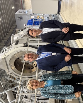 Cécile Neven, Olivier Servais et François Lepot posent devant le banc d’essai BeCover. Ils sont dans un grand hangar. 