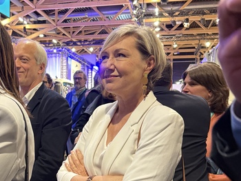 Photo de Cécile Neven souriante, les bras croisés, dans le public de l'inauguration du salon Municipalia. 