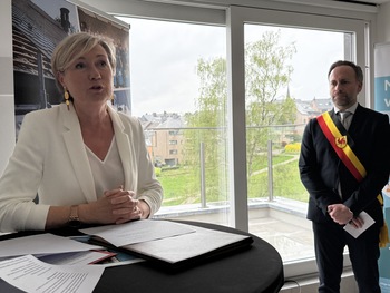 Cécile Neven prononce un discours d’inauguration dans un nouveau logement social lumineux et encore vide. Elle se tient aux côtés de Nicolas Van der Maren, bourgmestre d’Ottignies-Louvain-la-Neuve.
