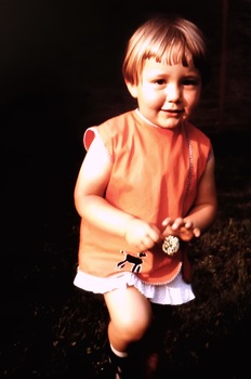  Cécile Neven lorsqu'elle était enfant, portant une robe orange et tenant une fleur à la main